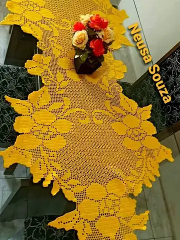 Caminho de mesa amarelo de crochê filet com flores, sobre mesa de vidro com um vaso de rosas