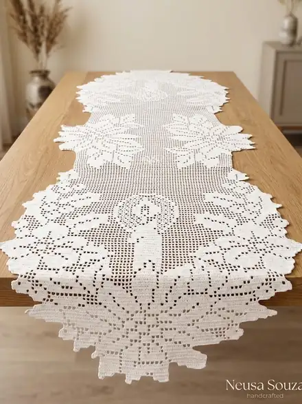 Caminho de mesa branco de crochê filet com velas e flores, estendido sobre mesa de madeira