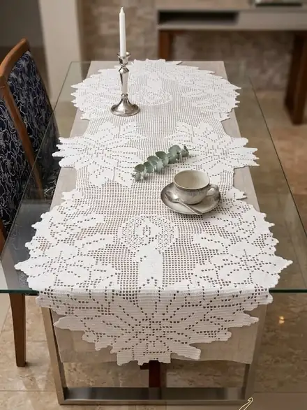 Caminho de mesa branco de crochê filet com velas e flores, sobre mesa de vidro com castiçal e xícara