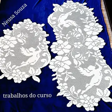 Duas peças brancas de crochê filet com pássaros e flores, sobre tecido azul